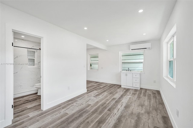 unfurnished bedroom featuring connected bathroom, light hardwood / wood-style flooring, and a wall unit AC