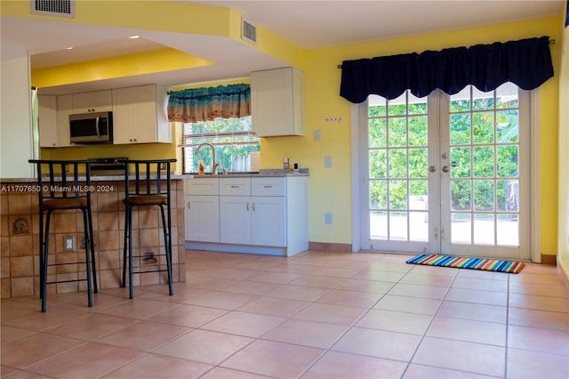 kitchen featuring light tile patterned floors, white cabinetry, a wealth of natural light, and french doors