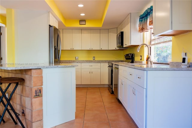 kitchen with a breakfast bar, white cabinets, light tile patterned floors, appliances with stainless steel finishes, and light stone counters