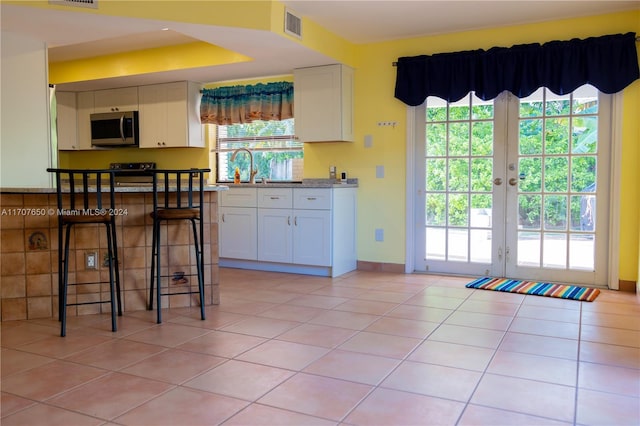 kitchen with a wealth of natural light, white cabinetry, french doors, and light tile patterned flooring