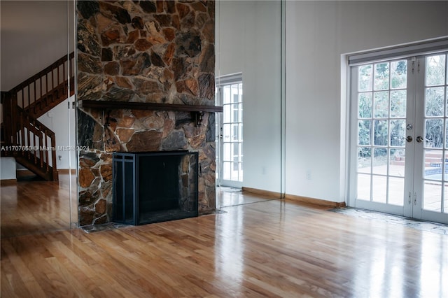 unfurnished living room with a stone fireplace, hardwood / wood-style floors, a high ceiling, and french doors