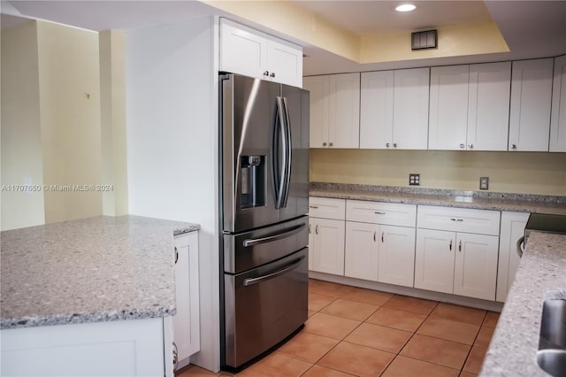 kitchen with white cabinetry, a raised ceiling, stainless steel fridge with ice dispenser, and light stone counters