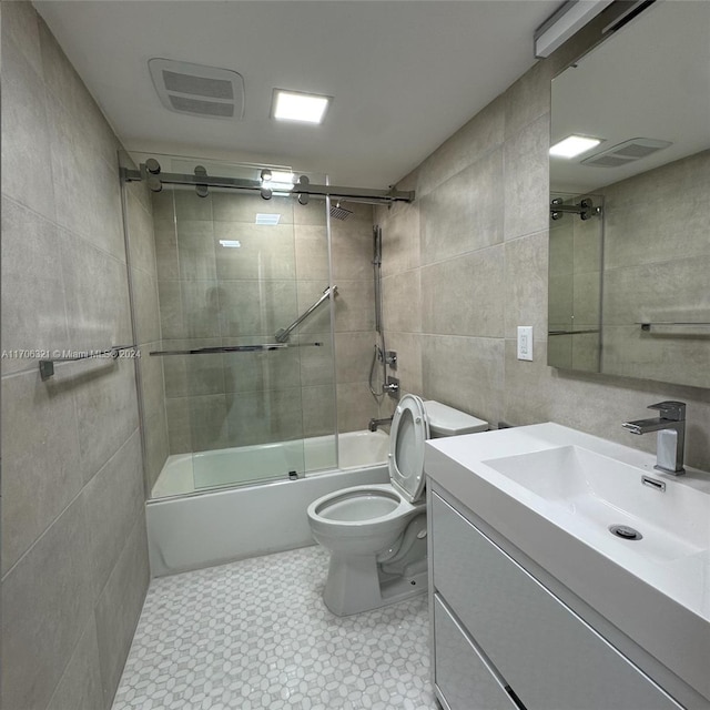 full bathroom with combined bath / shower with glass door, vanity, toilet, and tile walls