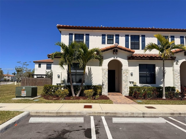 mediterranean / spanish-style house with a tile roof, uncovered parking, stone siding, and stucco siding