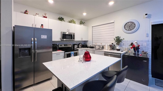 kitchen with a breakfast bar, a sink, a center island, appliances with stainless steel finishes, and light tile patterned floors