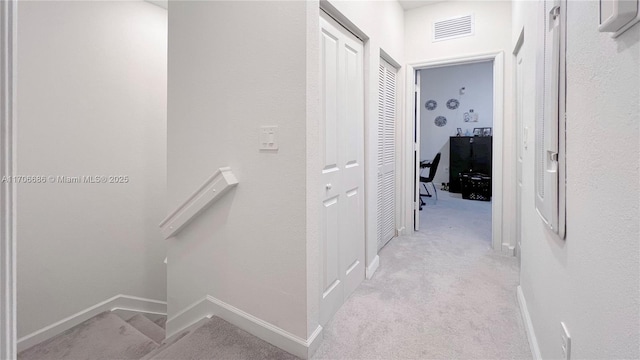 hall featuring visible vents, an upstairs landing, light colored carpet, and baseboards