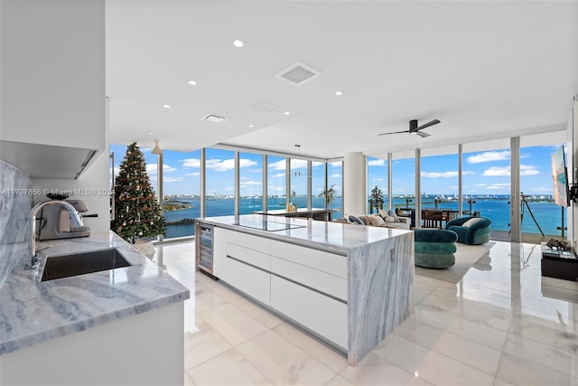 kitchen featuring floor to ceiling windows, white cabinets, sink, ceiling fan, and light stone countertops