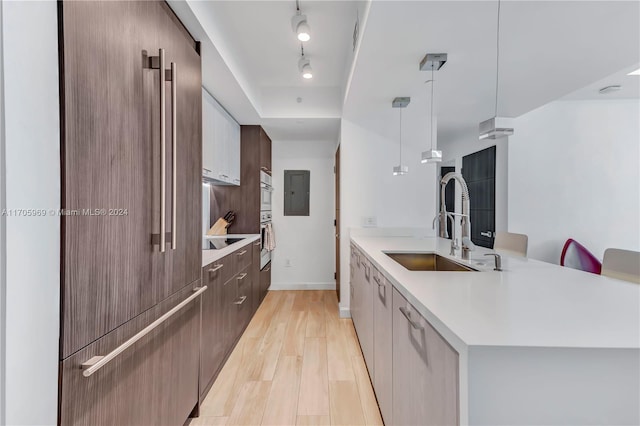 kitchen featuring sink, hanging light fixtures, light wood-type flooring, double oven, and kitchen peninsula