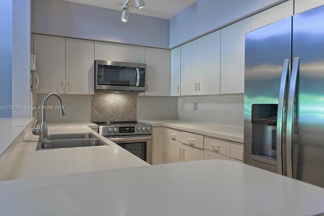 kitchen featuring track lighting, sink, decorative backsplash, appliances with stainless steel finishes, and white cabinetry