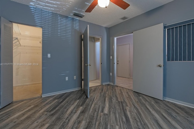 unfurnished bedroom with ceiling fan, dark wood-type flooring, a textured ceiling, a walk in closet, and a closet