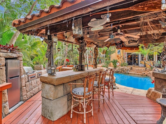 wooden terrace with ceiling fan, area for grilling, a bar, and exterior kitchen