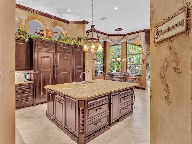 kitchen with decorative light fixtures, a notable chandelier, sink, crown molding, and a kitchen island with sink