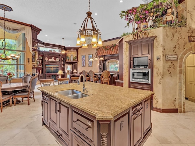 kitchen featuring pendant lighting, an inviting chandelier, an island with sink, sink, and stainless steel microwave