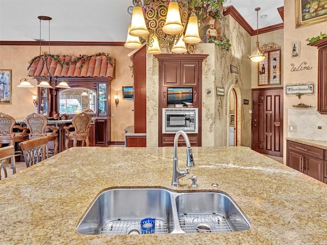 kitchen with decorative backsplash, sink, crown molding, hanging light fixtures, and light stone counters