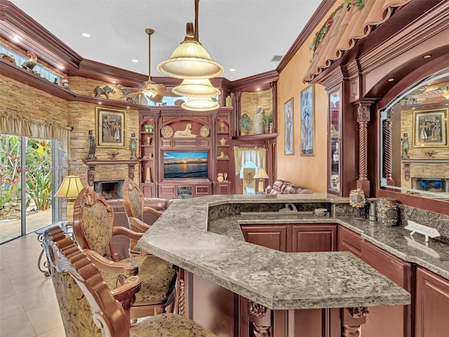 kitchen with decorative light fixtures, a breakfast bar, crown molding, a stone fireplace, and light tile patterned floors