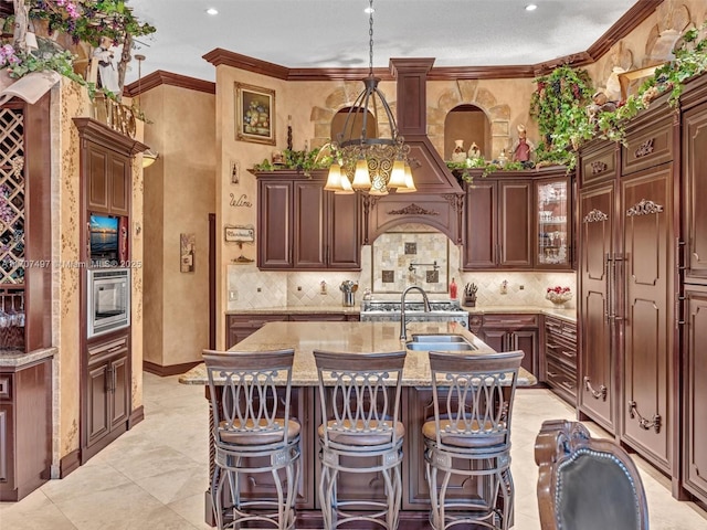 kitchen with ornamental molding, stainless steel microwave, a sink, and an island with sink