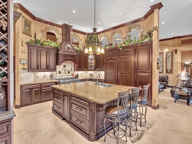 kitchen featuring light stone counters, crown molding, a center island with sink, a sink, and a kitchen breakfast bar