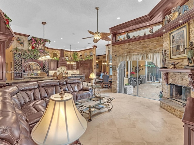 living area with a ceiling fan, ornamental molding, a textured ceiling, and a stone fireplace