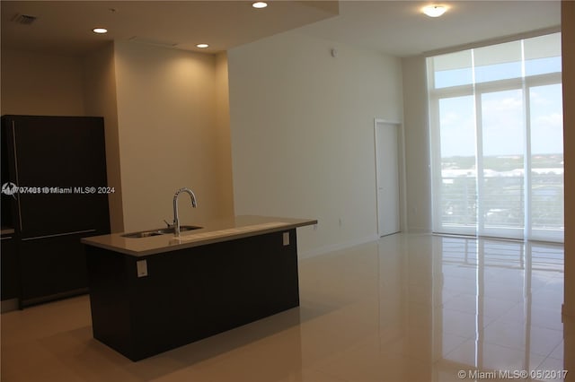 kitchen featuring light tile patterned flooring, sink, a wall of windows, and an island with sink