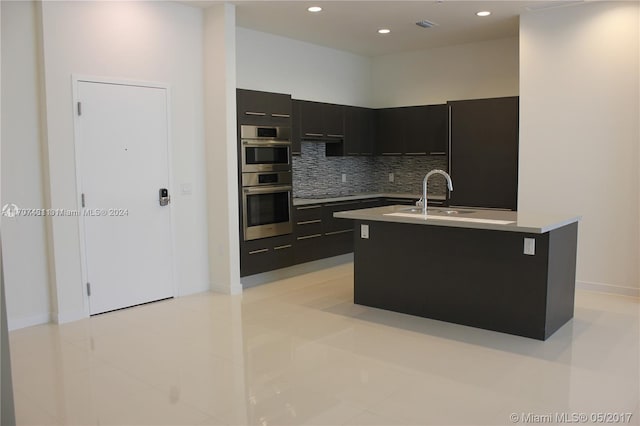 kitchen featuring backsplash, sink, light tile patterned floors, an island with sink, and double oven