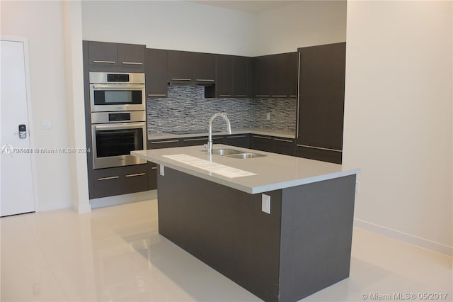 kitchen featuring decorative backsplash, double oven, sink, light tile patterned floors, and an island with sink