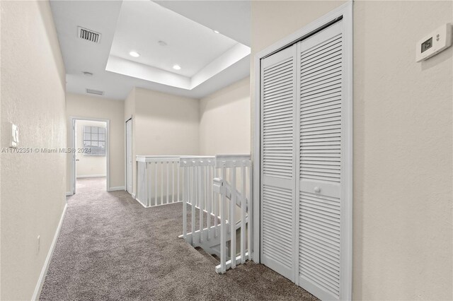 corridor featuring carpet floors and a raised ceiling