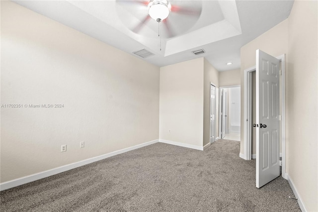 carpeted empty room with a raised ceiling and ceiling fan