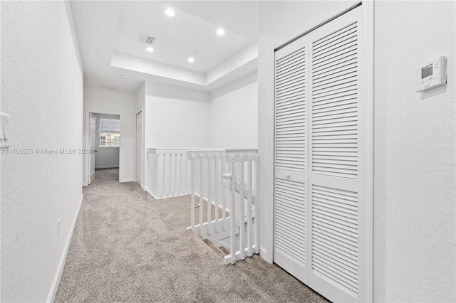 hall featuring light colored carpet and a raised ceiling