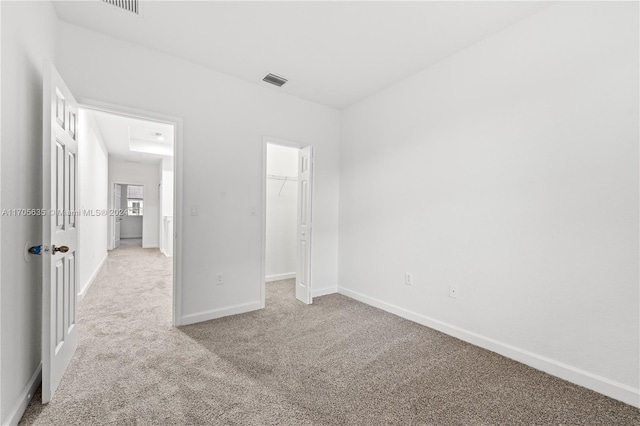 unfurnished bedroom with light carpet, a closet, and a spacious closet