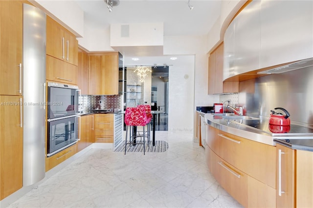 kitchen with backsplash, double oven, stainless steel counters, stainless steel stovetop, and light brown cabinets