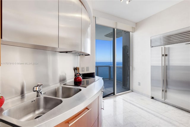 kitchen featuring black electric cooktop, a water view, built in fridge, and sink