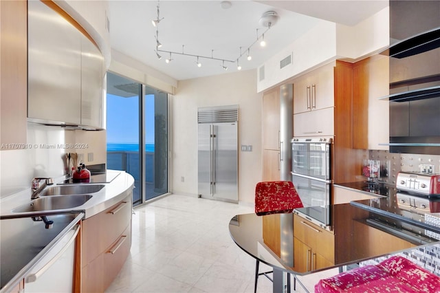 kitchen featuring a water view, rail lighting, sink, appliances with stainless steel finishes, and tasteful backsplash