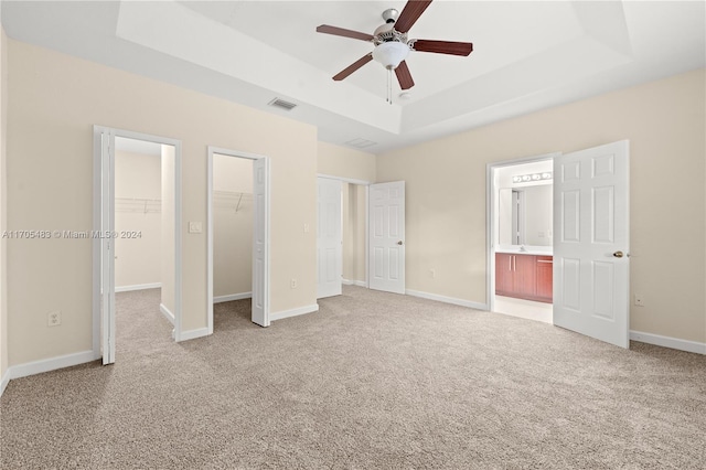 unfurnished bedroom featuring connected bathroom, ceiling fan, a spacious closet, a raised ceiling, and light colored carpet