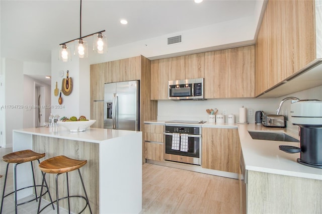 kitchen with hanging light fixtures, sink, light wood-type flooring, light brown cabinetry, and appliances with stainless steel finishes