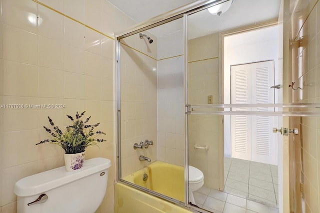 bathroom with tile patterned floors, bath / shower combo with glass door, tile walls, and toilet