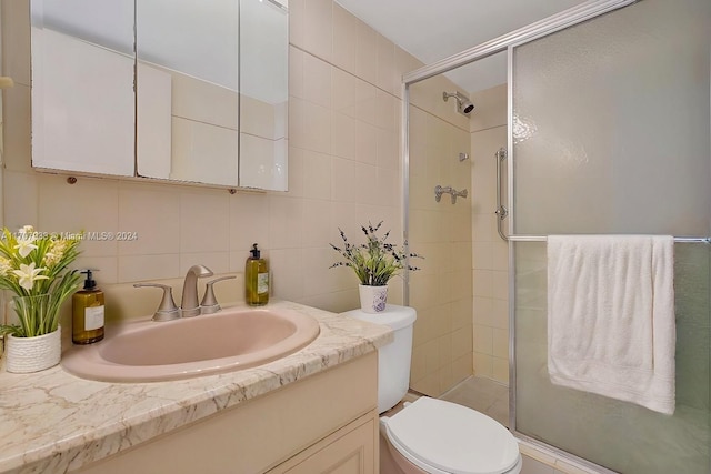 bathroom featuring vanity, a shower with door, toilet, tile walls, and tasteful backsplash