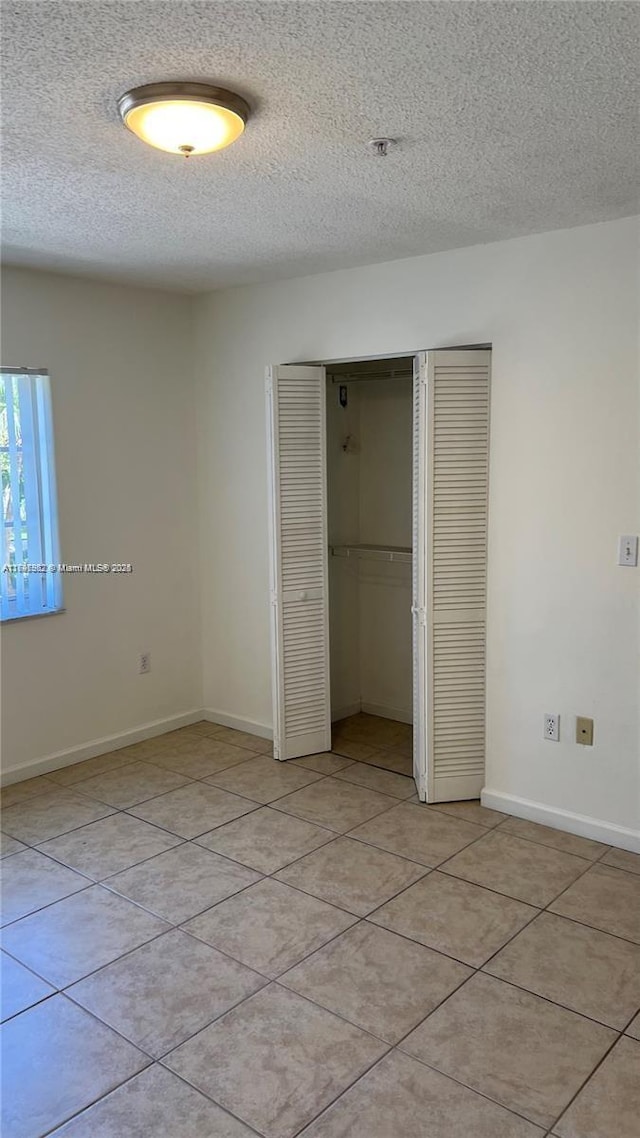 unfurnished bedroom with light tile patterned floors, a closet, and a textured ceiling