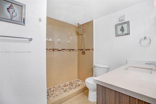 bathroom with tile patterned flooring, vanity, toilet, and tiled shower