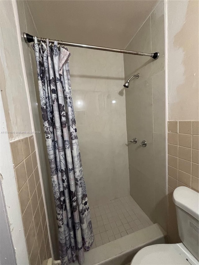 bathroom with a shower with shower curtain, toilet, and tile walls