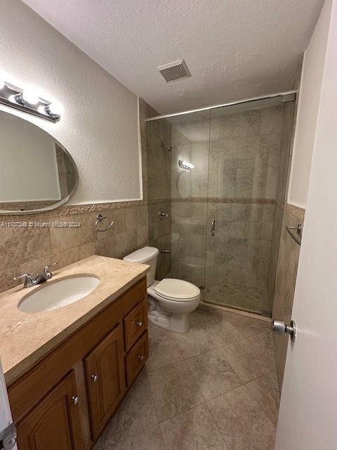 bathroom featuring vanity, toilet, a textured ceiling, tile walls, and an enclosed shower