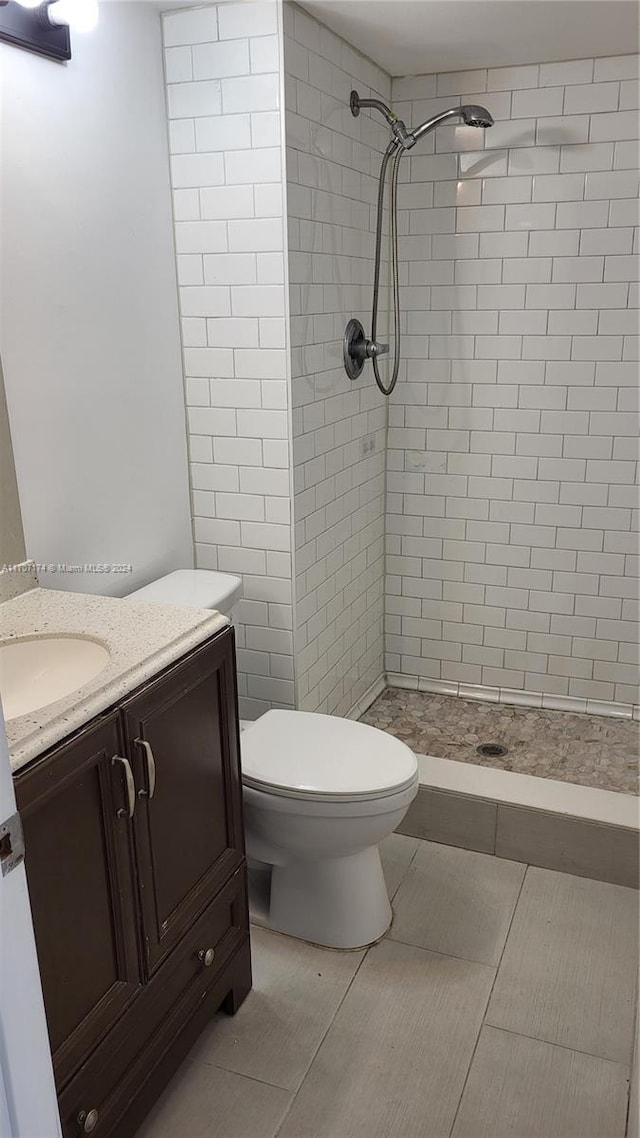 bathroom with a tile shower, vanity, toilet, and tile patterned floors