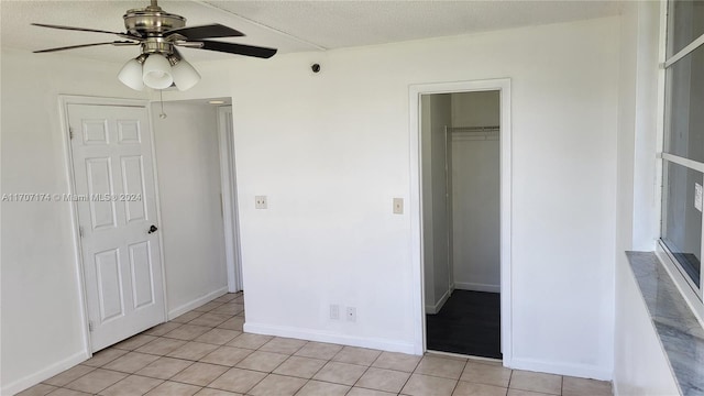 unfurnished bedroom featuring ceiling fan, a spacious closet, a textured ceiling, light tile patterned flooring, and a closet