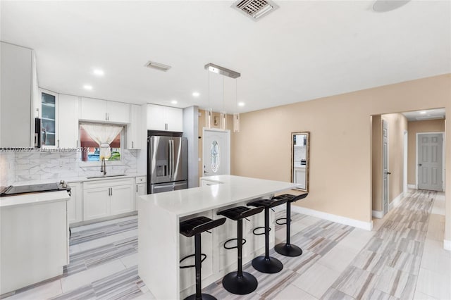 kitchen featuring a center island, sink, hanging light fixtures, stainless steel fridge, and white cabinets