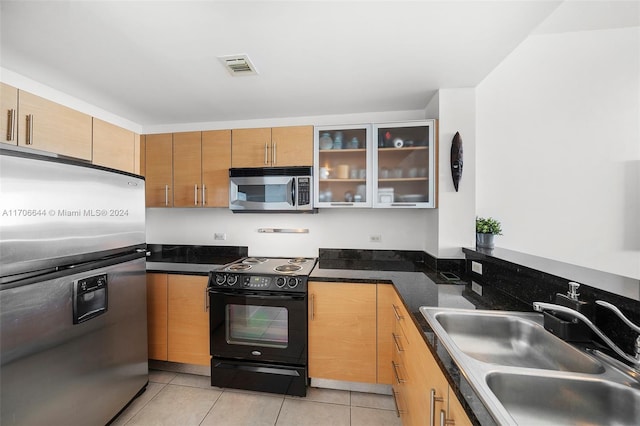 kitchen featuring light tile patterned flooring, appliances with stainless steel finishes, dark stone countertops, and sink