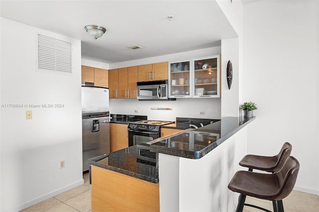 kitchen featuring dark stone countertops, light tile patterned floors, a kitchen bar, kitchen peninsula, and stainless steel appliances