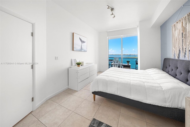 bedroom featuring a water view, light tile patterned flooring, and track lighting