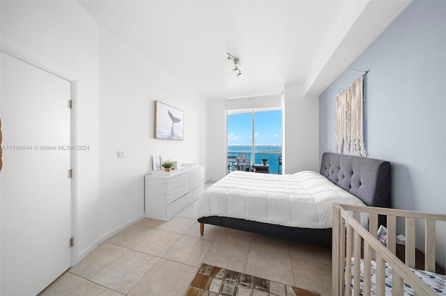 bedroom featuring light tile patterned flooring, a water view, and rail lighting