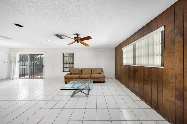 living room with wooden walls, ceiling fan, light tile patterned flooring, and a textured ceiling