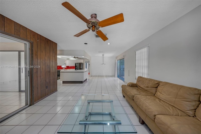 living room with ceiling fan, a textured ceiling, and wooden walls