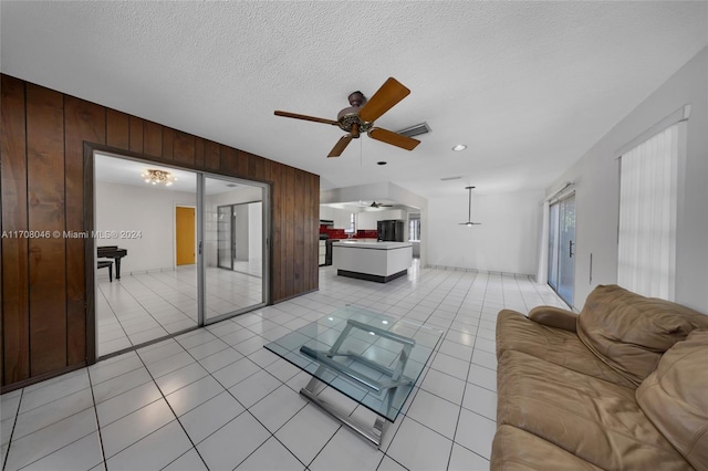 living room featuring a textured ceiling, ceiling fan, light tile patterned floors, and wood walls